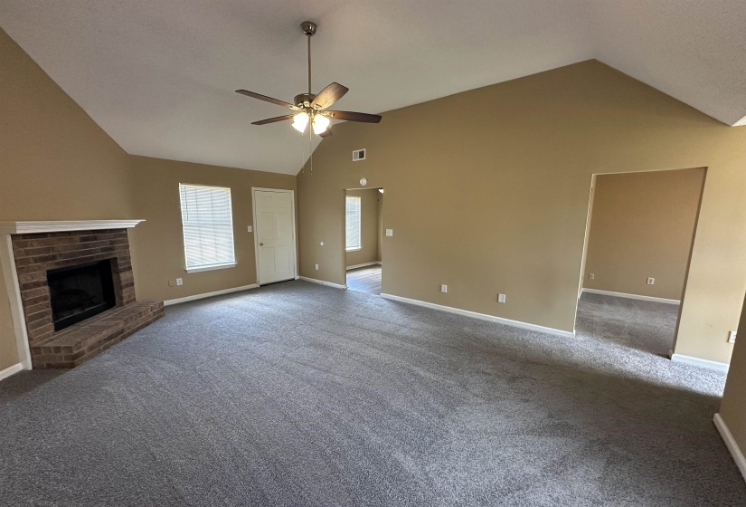 Living room featuring vaulted ceilings, a brick fireplace, a ceiling fan with integrated lighting, and neutral-toned carpeting