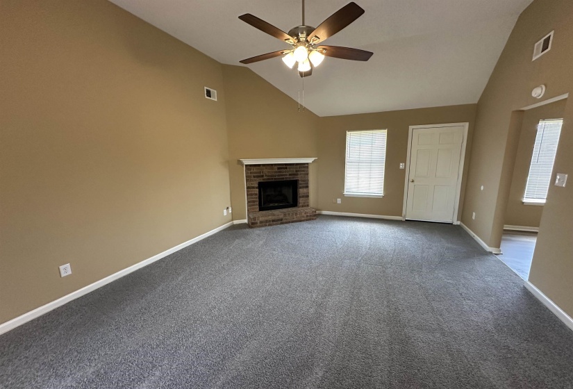 Spacious room featuring vaulted ceilings, a brick fireplace with a white mantel, and neutral-toned carpeting