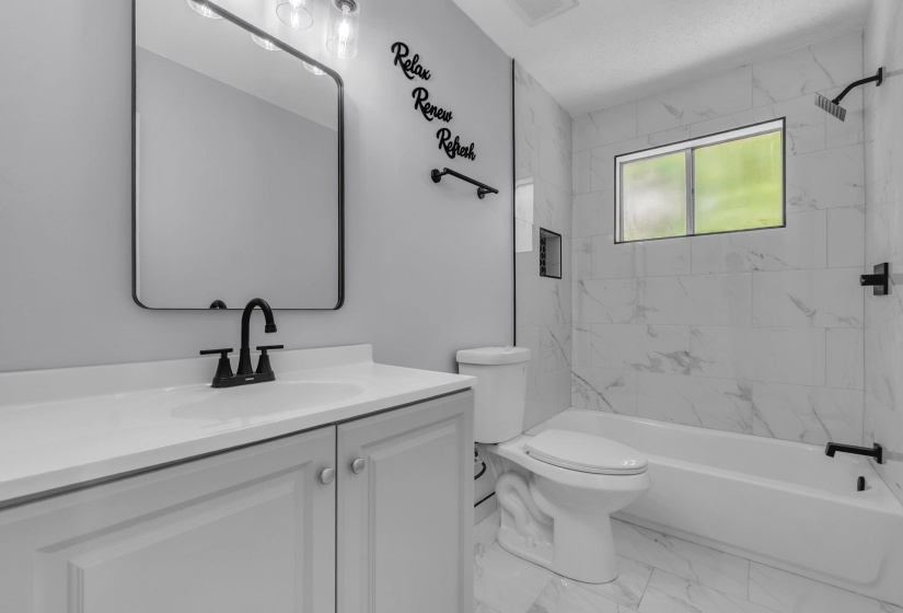 Bathroom featuring a white vanity with integrated sink, black fixtures, and a framed mirror