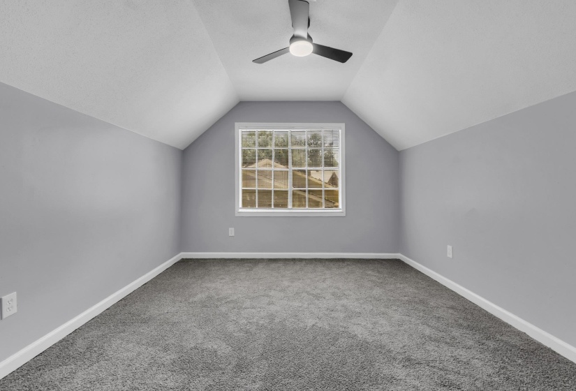 Vaulted ceiling room featuring a central window, ceiling fan, plush grey carpet, and light grey wall finishes with white trim