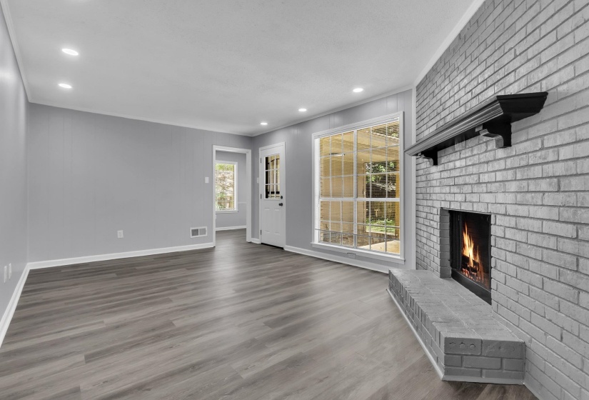 Spacious living area featuring a gray brick fireplace with a dark wood mantel, large multi-pane windows, and wood-finish flooring