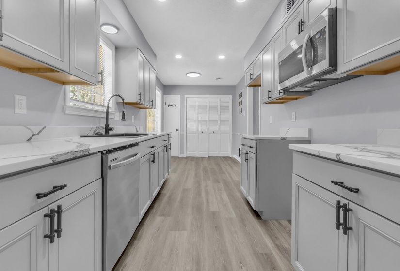 Modern kitchen featuring light gray shaker cabinetry with dark hardware, white countertops with veining, and wood-finish flooring