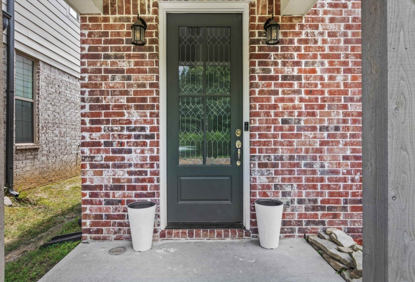 Front entry featuring a leaded glass door, brick facade, wall sconces, concrete porch, and vertical wood siding