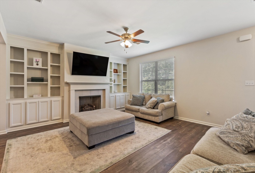 Living area featuring a fireplace with a mantel, built-in shelving, wood-finish flooring, and a ceiling fan