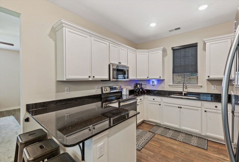 Kitchen featuring white cabinetry, dark stone countertops, stainless steel appliances, wood-finish flooring, and recessed lighting