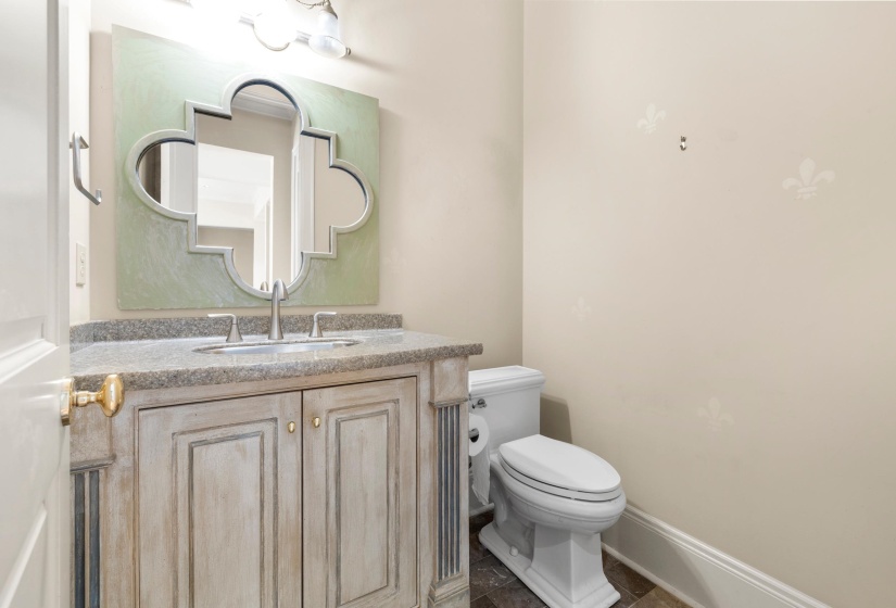 Powder room featuring a custom vanity with a stone countertop, an undermount sink with a brushed nickel faucet, an ornate mirror, and a contemporary toilet
