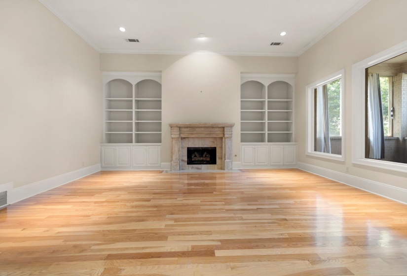 Hardwood flooring throughout featuring a stone-clad fireplace with a black firebox, flanked by two built-in arched bookcases with lower cabinetry, and recessed lighting
