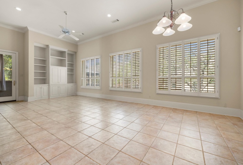 Spacious room with large-format tile flooring, built-in white cabinetry, two windows with plantation shutters, a glass-paned door, and high ceilings with recessed lighting