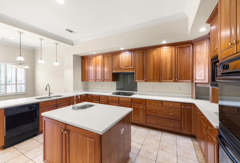 Kitchen featuring wood cabinetry, light-toned countertops, a central island with a sink, stainless steel double basin sink, and tile flooring