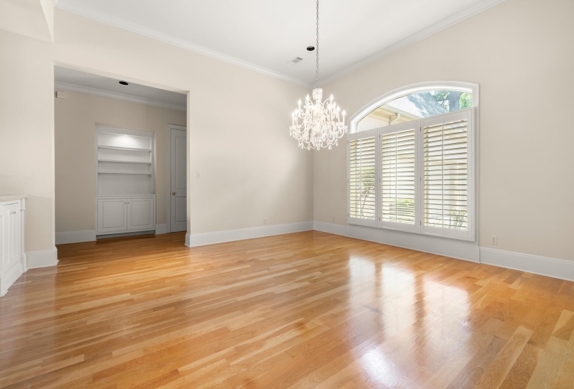 Bright interior space featuring wood-finish flooring, a crystal chandelier, an arched window with plantation shutters, crown molding, and built-in shelving with cabinetry