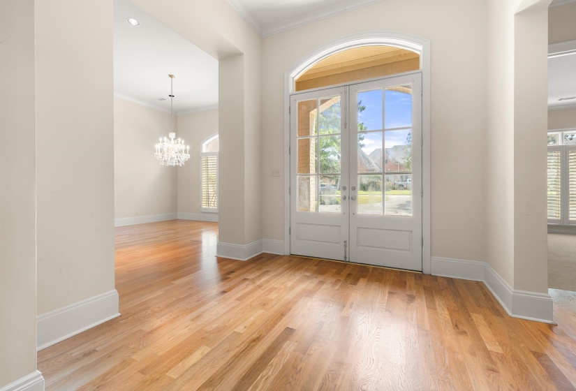Foyer with hardwood flooring, arched double entry doors, high ceilings, crown molding, and a visible chandelier in an adjacent room
