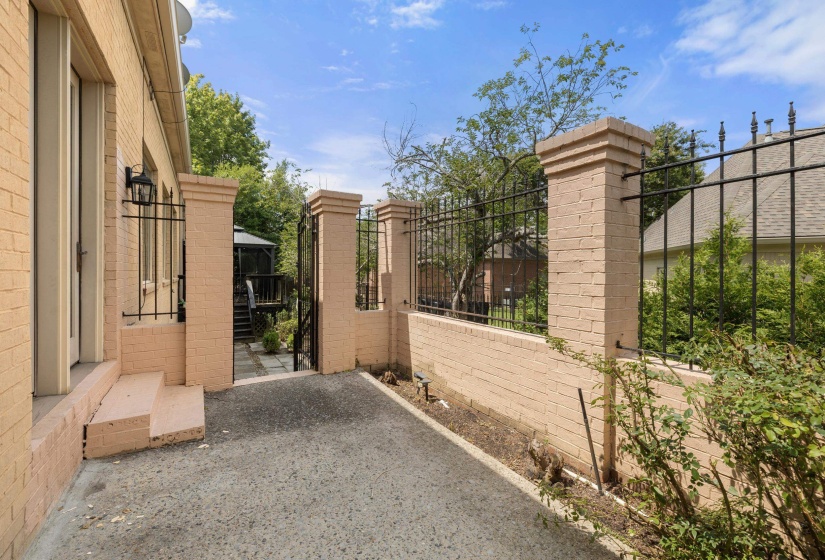 Tan brick exterior featuring a black iron fence with brick pillars, a side entry door, and a paved pathway