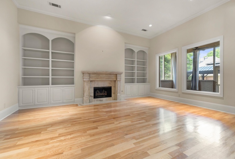 Spacious interior featuring wood-finish flooring, a stone-surround fireplace, built-in shelving, high ceilings, and recessed lighting