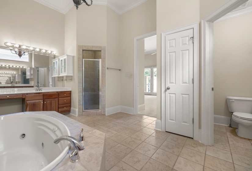 Bathroom featuring a large corner soaking tub with chrome fixtures, a spacious double vanity with wood cabinetry and an integrated makeup area, a separate tiled shower enclosure with a glass door, and square tiled flooring