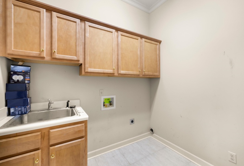 Utility room featuring a built-in sink with stainless steel basin, light wood-finish cabinetry, and light-toned floor tiling