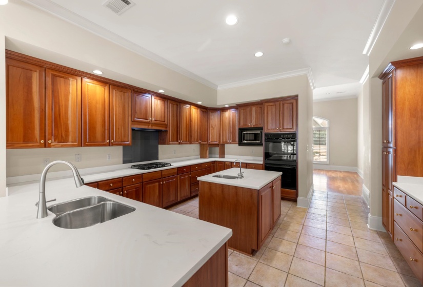 Spacious kitchen featuring extensive wood cabinetry, light-toned countertops, and a central island with a prep sink