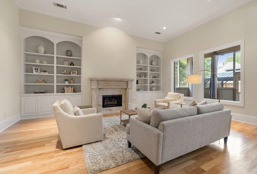 Living space featuring hardwood flooring, a stone fireplace, built-in shelving, high ceilings, and multiple windows