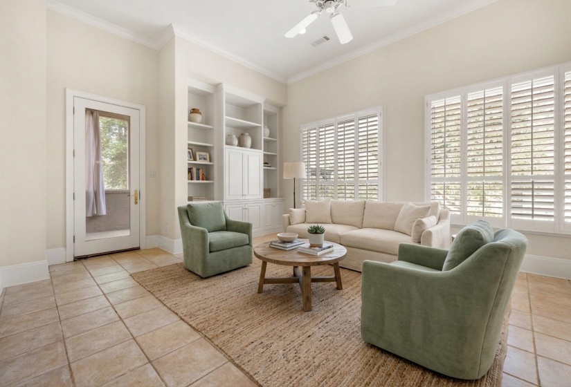 Living area featuring tiled flooring, built-in shelving, white plantation shutters, and a ceiling fan