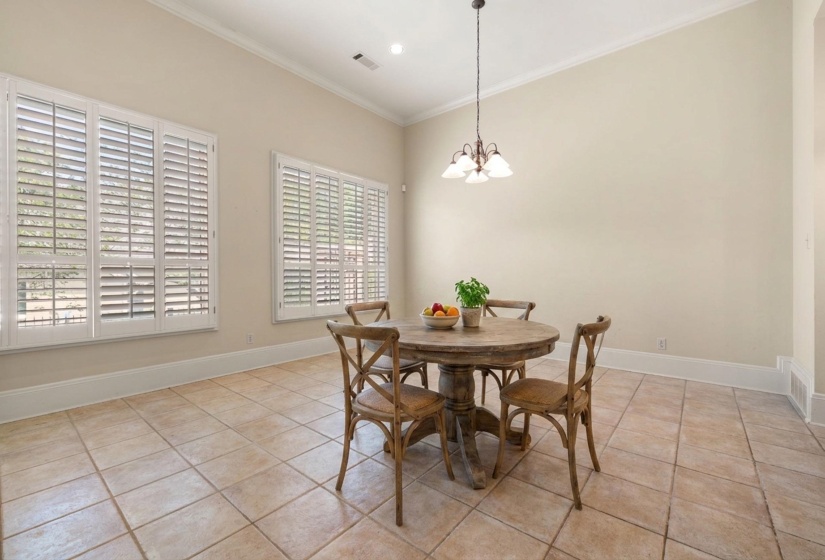 Spacious dining area featuring neutral wall tones, tile flooring, and vaulted ceilings with crown molding