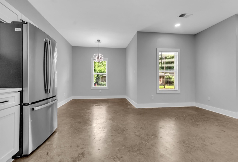 Open-concept living space featuring a stainless steel refrigerator, white cabinetry, light gray walls, concrete flooring, and recessed lighting