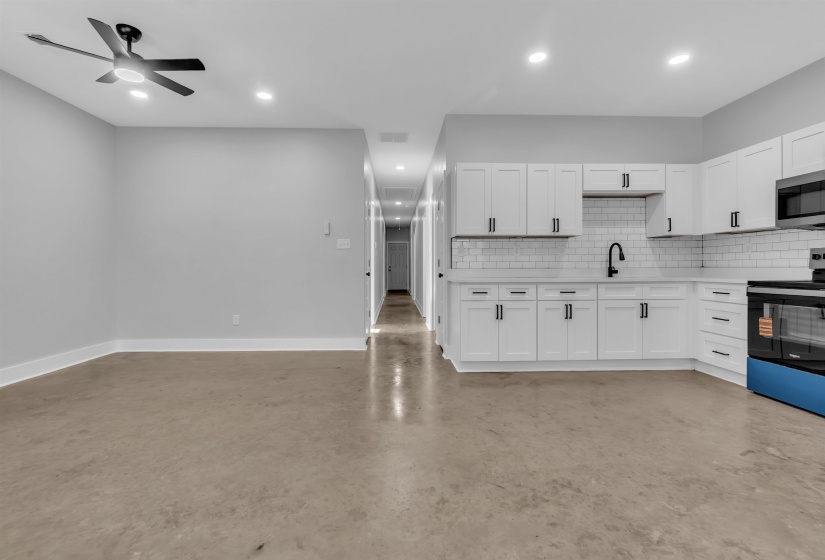 Open-concept living area featuring a modern kitchen with white cabinetry, subway tile backsplash, and dark hardware