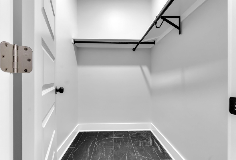 Efficient closet space featuring dark tile flooring, white walls, built-in shelving, and a hanging rod