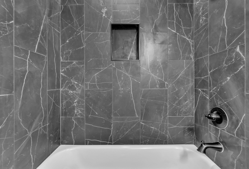 Bathtub enclosure featuring dark, veined wall tile and an integrated shower niche