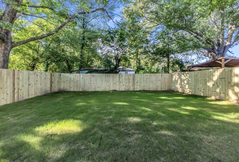Spacious backyard featuring a new privacy fence, mature trees, and a grassy lawn
