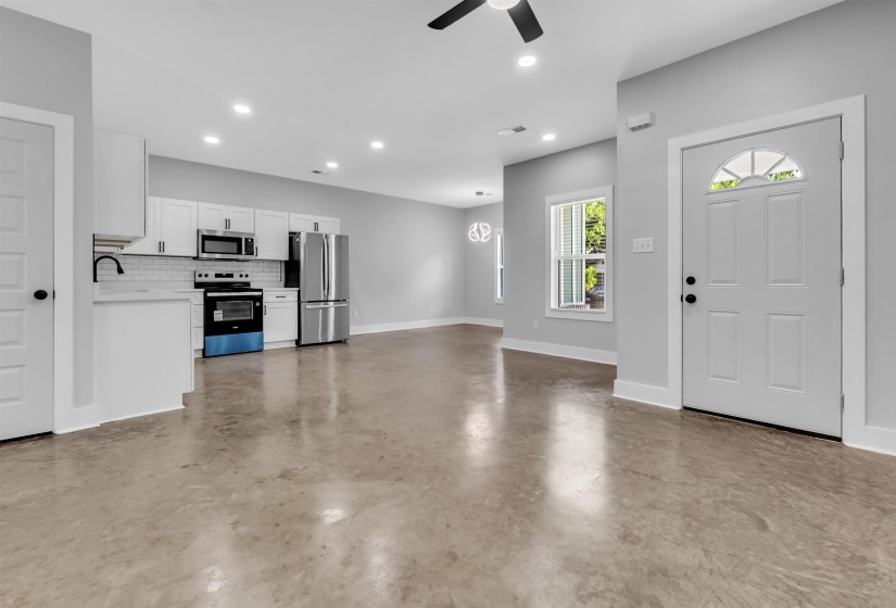 Open-concept living area featuring a modern kitchen with white cabinetry, stainless steel appliances, and a subway tile backsplash