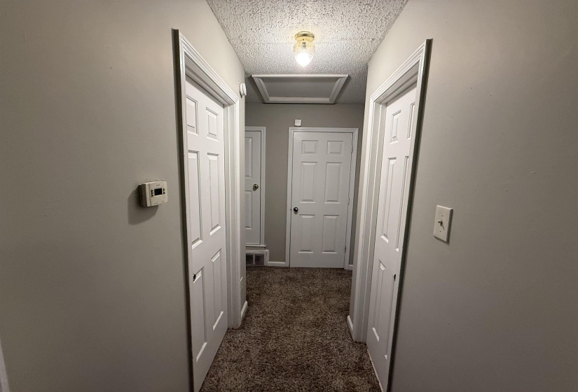 Hallway featuring neutral wall paint and textured carpeting