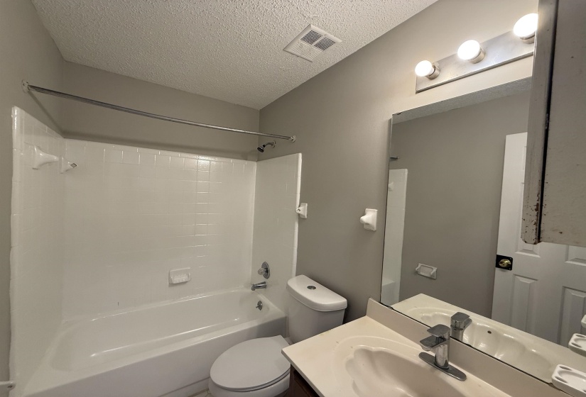 Bathroom featuring a white tub/shower combination with tiled surround, a white toilet, and a vanity with an integrated sink