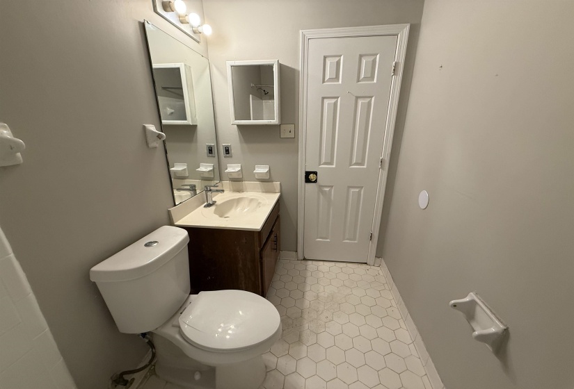 Bathroom featuring a hexagonal tile floor, a vanity with a white countertop and integrated sink, a wall-mounted mirror, and a recessed medicine cabinet