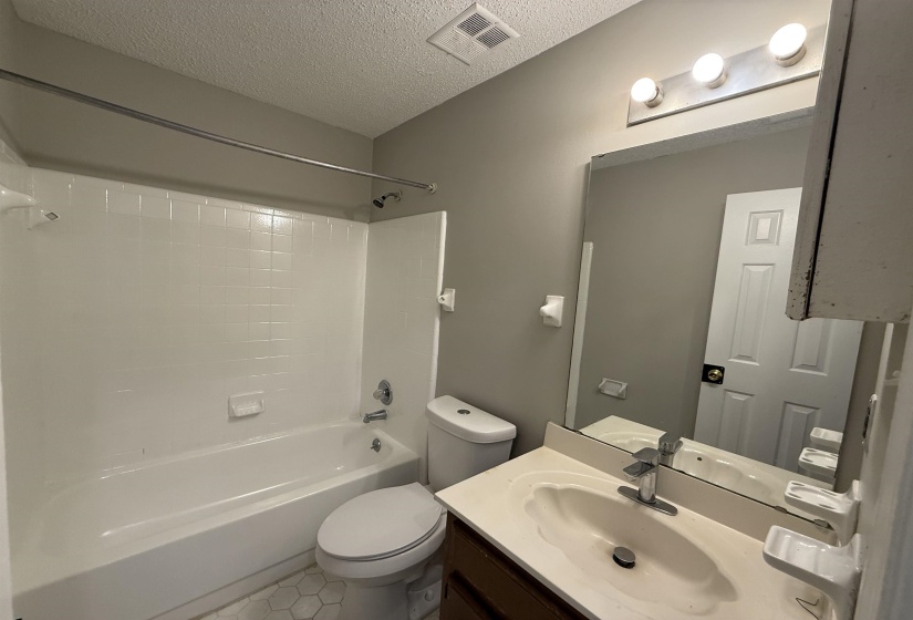 Full bathroom featuring a white tub/shower combination with chrome fixtures, a white toilet, and hexagonal floor tiling