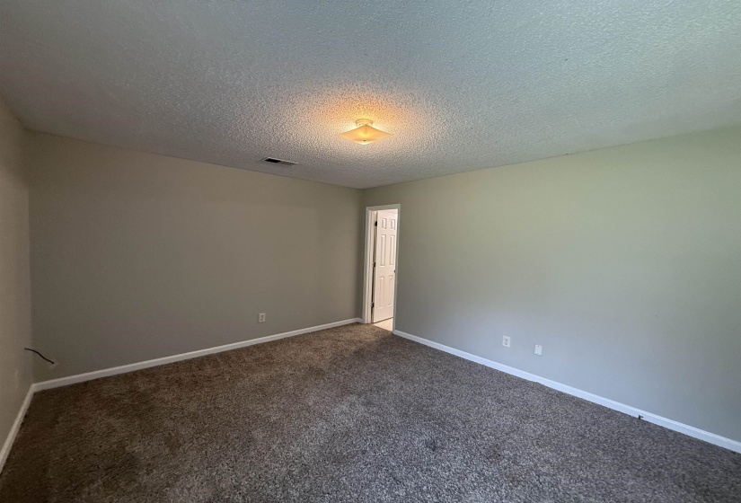 Spacious room featuring neutral painted walls, textured ceiling, and low-pile carpet flooring
