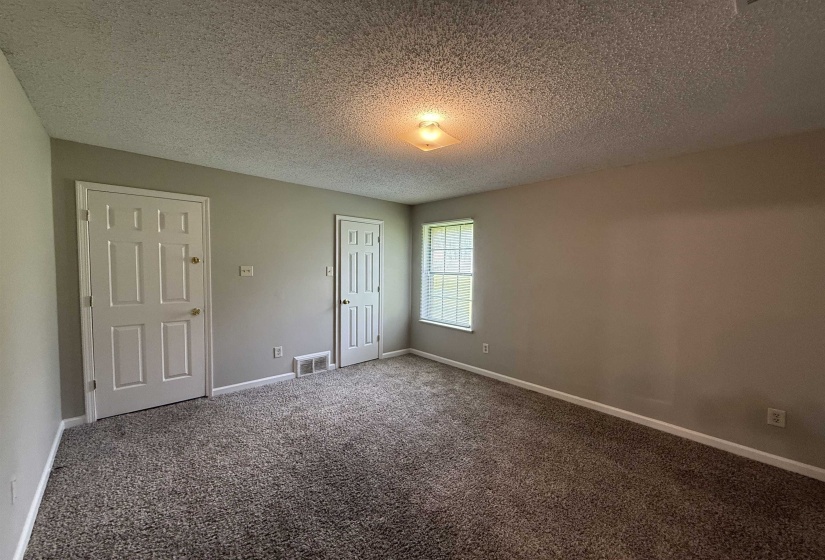 Neutral-toned room featuring a window with natural light, two panel doors, and a textured ceiling