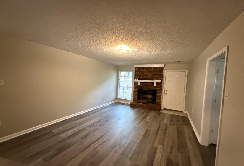 Living area featuring wood-finish flooring, a brick fireplace with a white mantel, neutral wall paint, and white trim