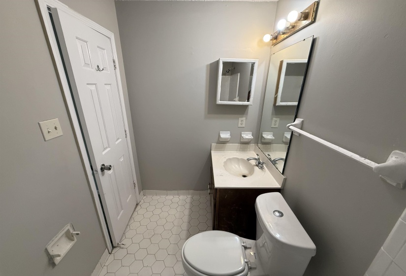 Compact bathroom featuring a white hexagonal tile floor, dark wood-finish vanity with a shell-shaped basin, a medicine cabinet, and a wall-mounted mirror