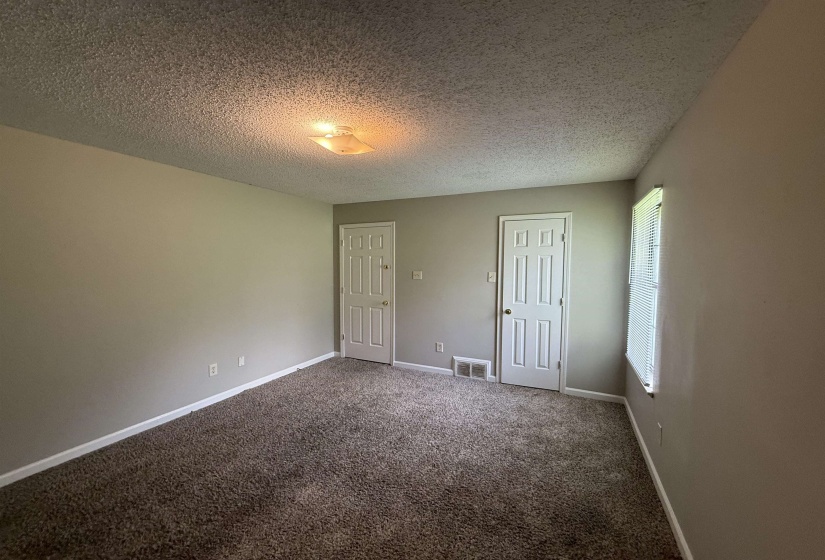 Spacious interior room with neutral-toned walls, brown textured carpeting, and white baseboards