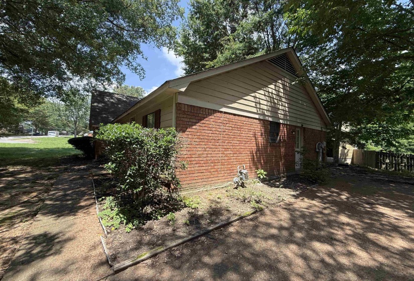 Brick and siding exterior featuring a pitched roofline and mature trees providing natural shade