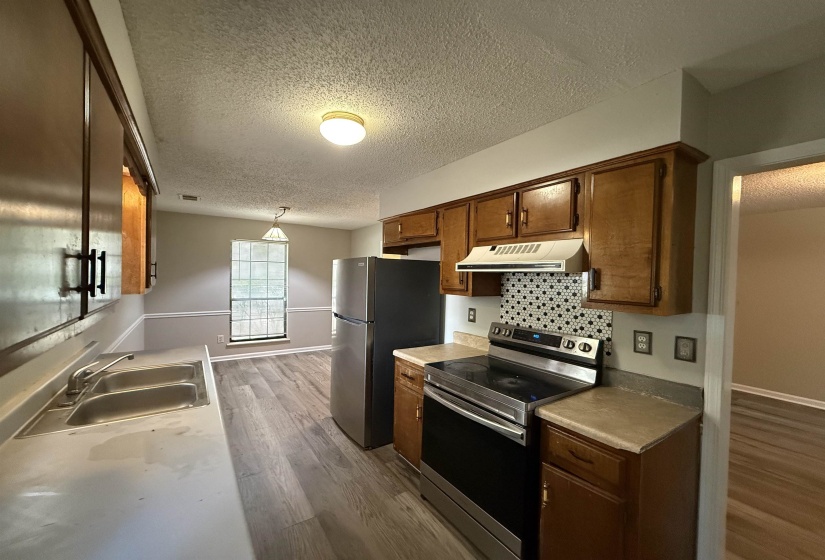 Kitchen featuring wood cabinetry, stainless steel appliances, a black and white geometric tile backsplash, and light wood-finish flooring