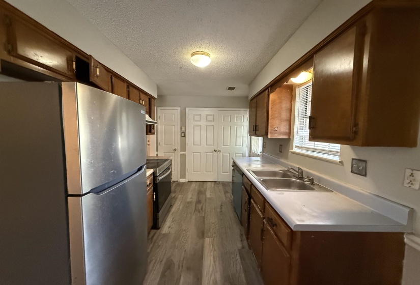 Galley kitchen featuring wood-finish cabinetry, light-toned countertops, and wood-finish flooring