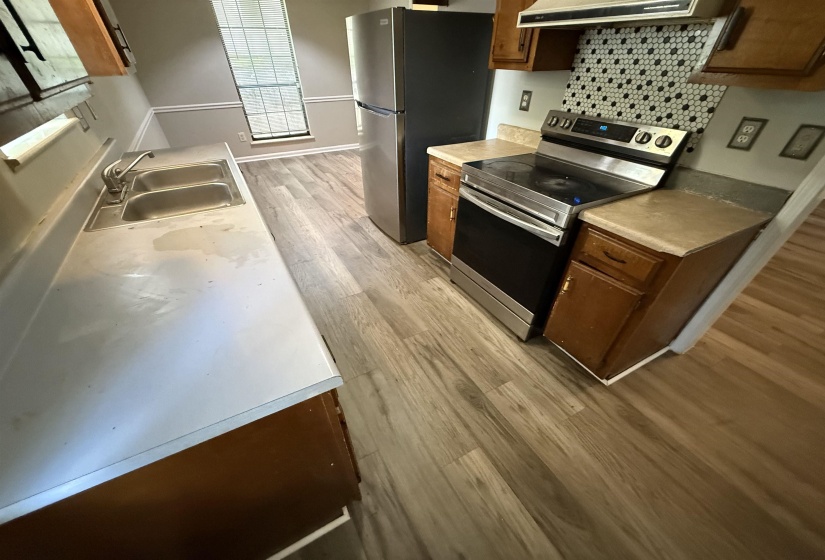 Kitchen featuring wood-finish flooring, a stainless steel electric range, a mosaic tile backsplash, a double basin sink, and a refrigerator