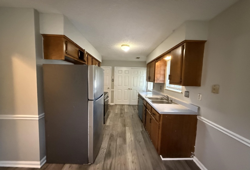 Galley kitchen featuring wood-finish flooring, wood cabinetry, a double basin stainless steel sink, and light countertops
