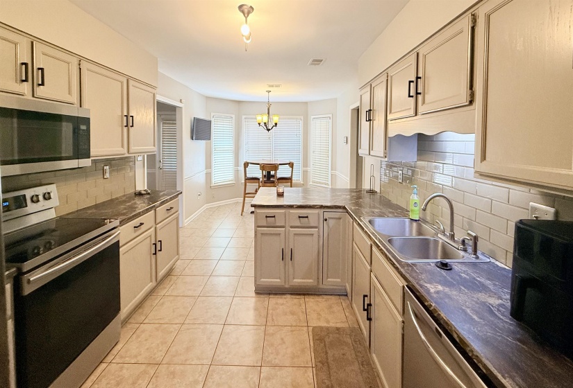 Kitchen featuring light-toned cabinetry with modern hardware, stainless steel appliances, tile flooring, and stone-look countertops