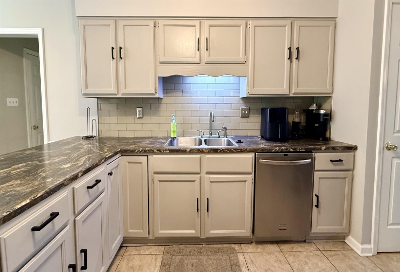 Updated kitchen featuring light-toned cabinetry with dark hardware, stone-look countertops, a subway tile backsplash, a double basin sink, and tile flooring