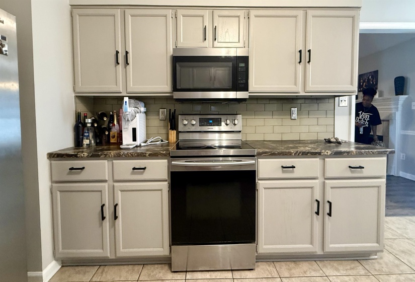 Kitchen featuring light-toned cabinetry with black hardware, stainless steel range, built-in microwave, subway tile backsplash, and patterned countertops