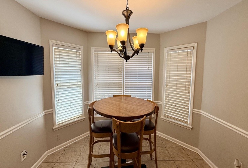 Bay window area featuring five windows with blinds, a bronze chandelier, chair rail molding, and tile flooring