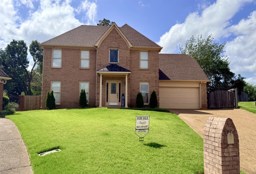Traditional brick residence featuring a two-car garage, established front lawn, and a covered entry porch supported by white columns