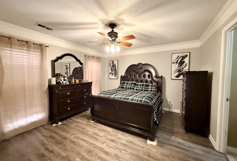 Spacious room featuring wood-finish flooring, crown molding, and a ceiling fan with integrated lighting