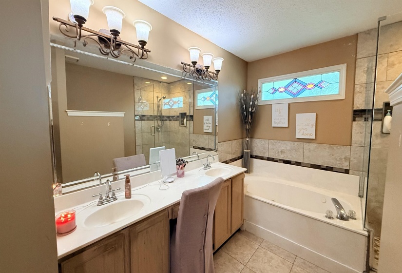 Bathroom featuring a double vanity with integrated sinks, a built-in jetted tub, a stained glass window accent, and a tiled shower enclosure